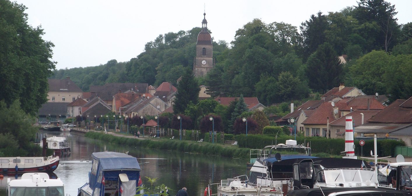 Port de plaisance, bateaux amarrés et maisons aux toits de tuiles devant une colline boisée